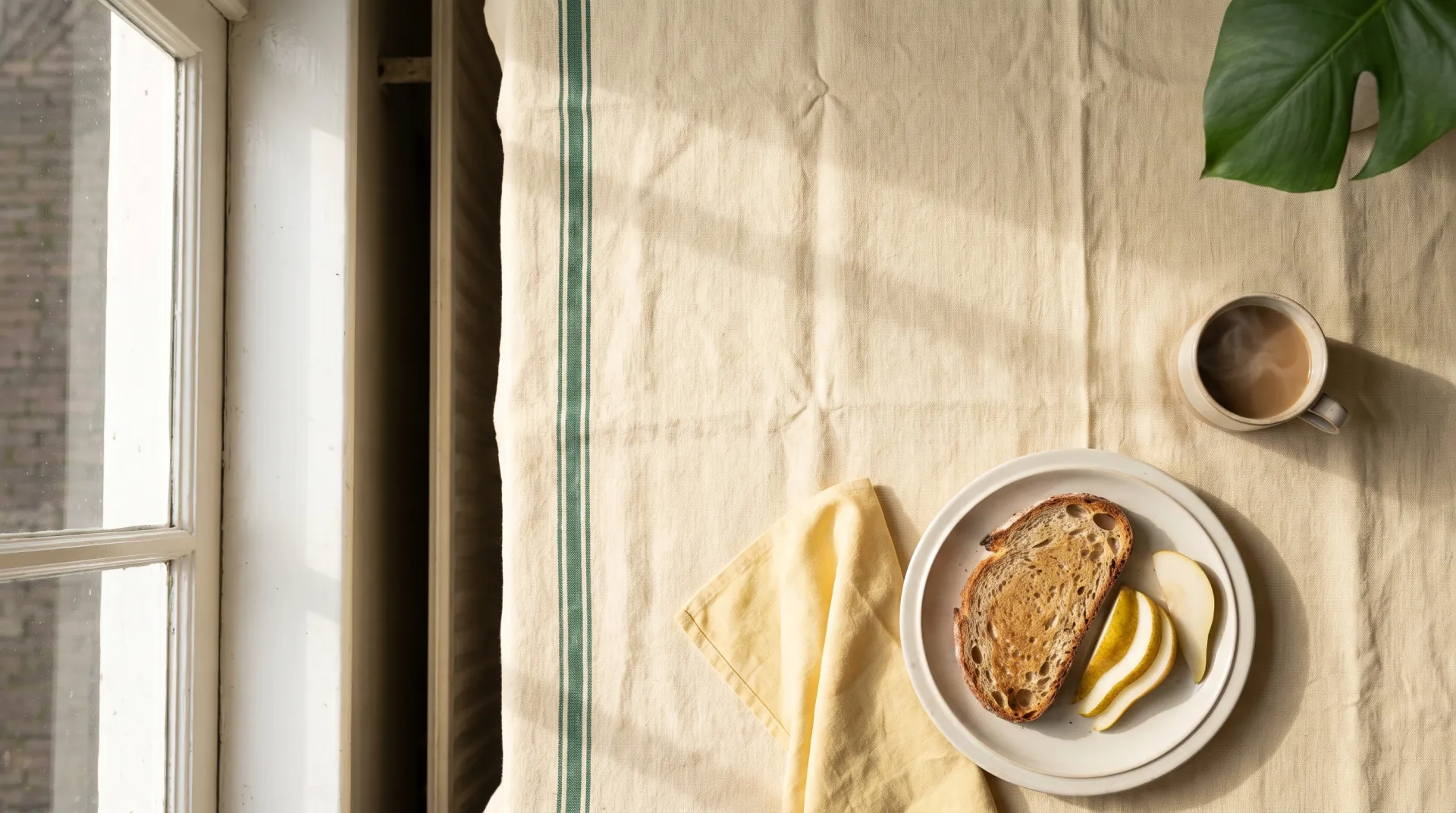 Illustrative sunlit brunch table with toast, pear and coffee on linen