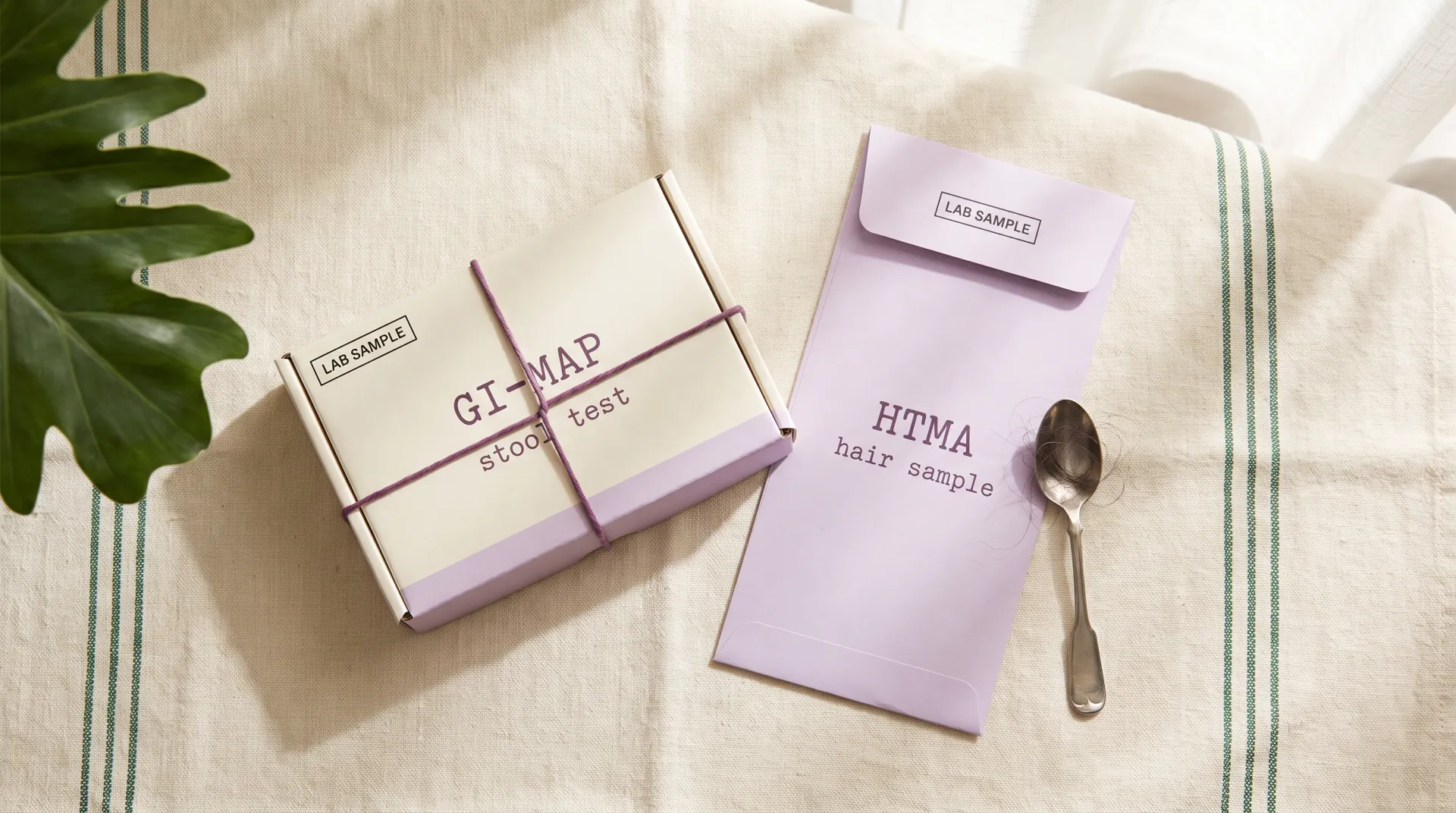 Illustrative GI-MAP stool-test box and HTMA hair-sample envelope on linen, not actual manufacturer packaging